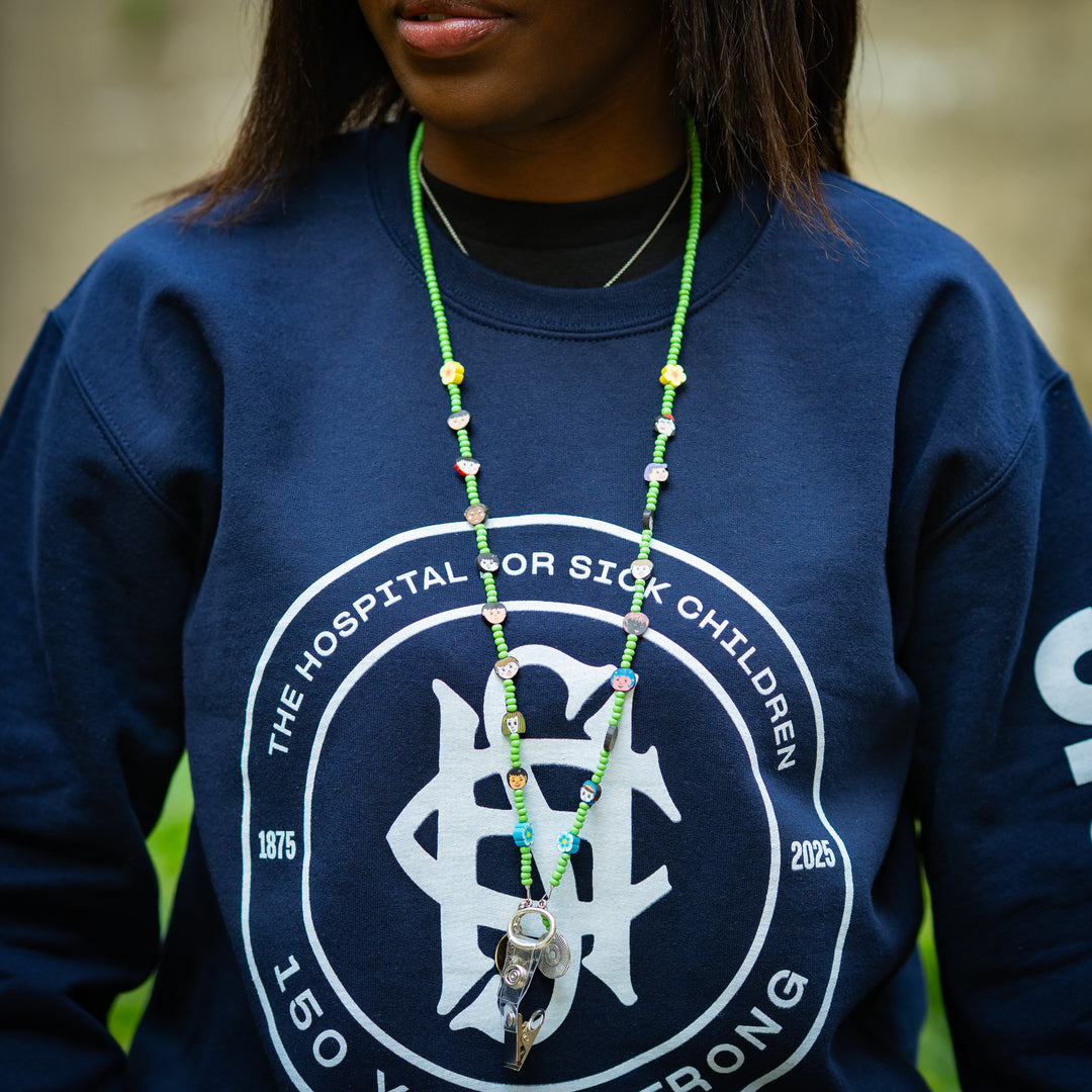 Person wearing a navy blue sweatshirt with a green beaded lanyard, standing outdoors.