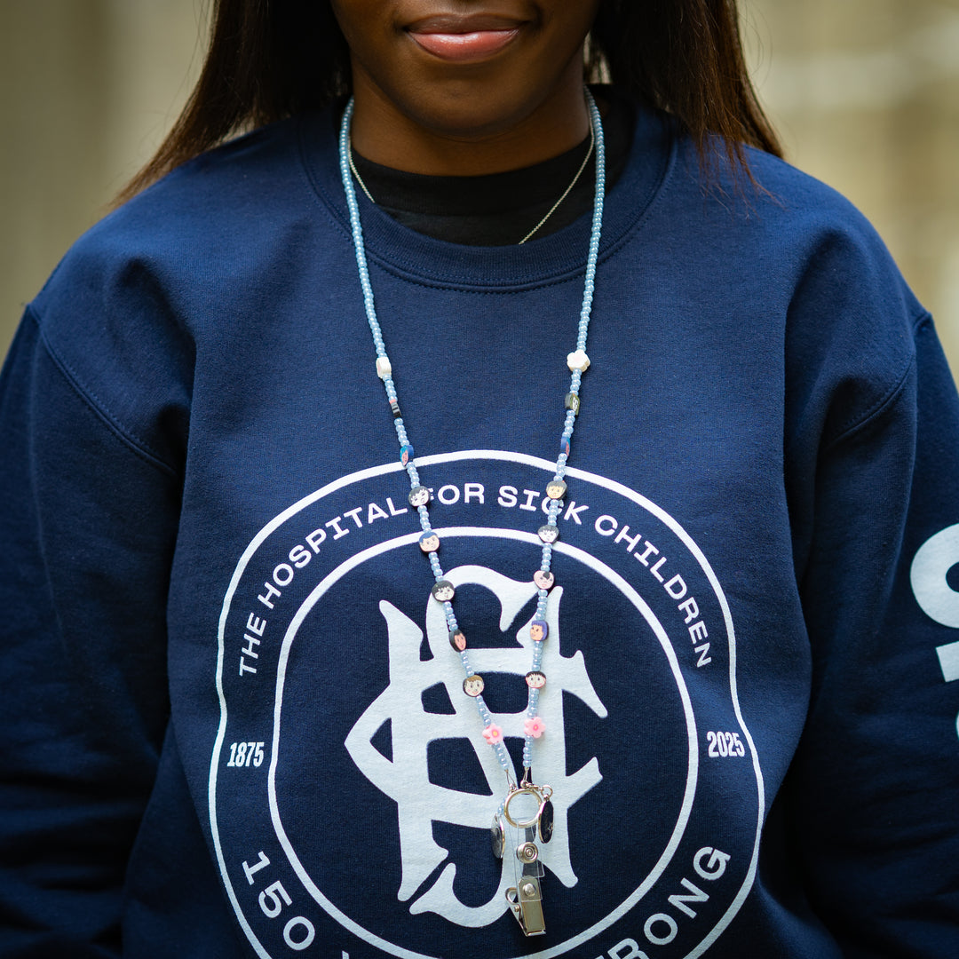 Person wearing a navy blue sweatshirt with a light blue beaded lanyard, standing outdoors.