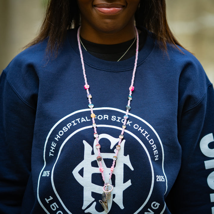 Person wearing a navy blue sweatshirt with a pink beaded lanyard, standing outdoors.