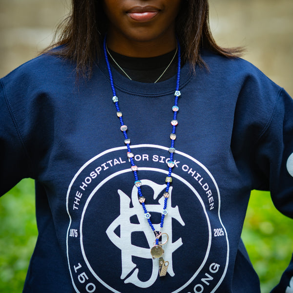 Person wearing a navy blue sweatshirt with a blue beaded lanyard, standing outdoors.