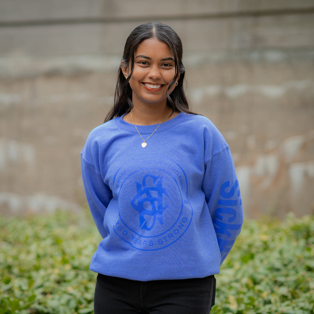 A person wearing a navy blue crewneck sweater with a logo on the chest standing outdoors.