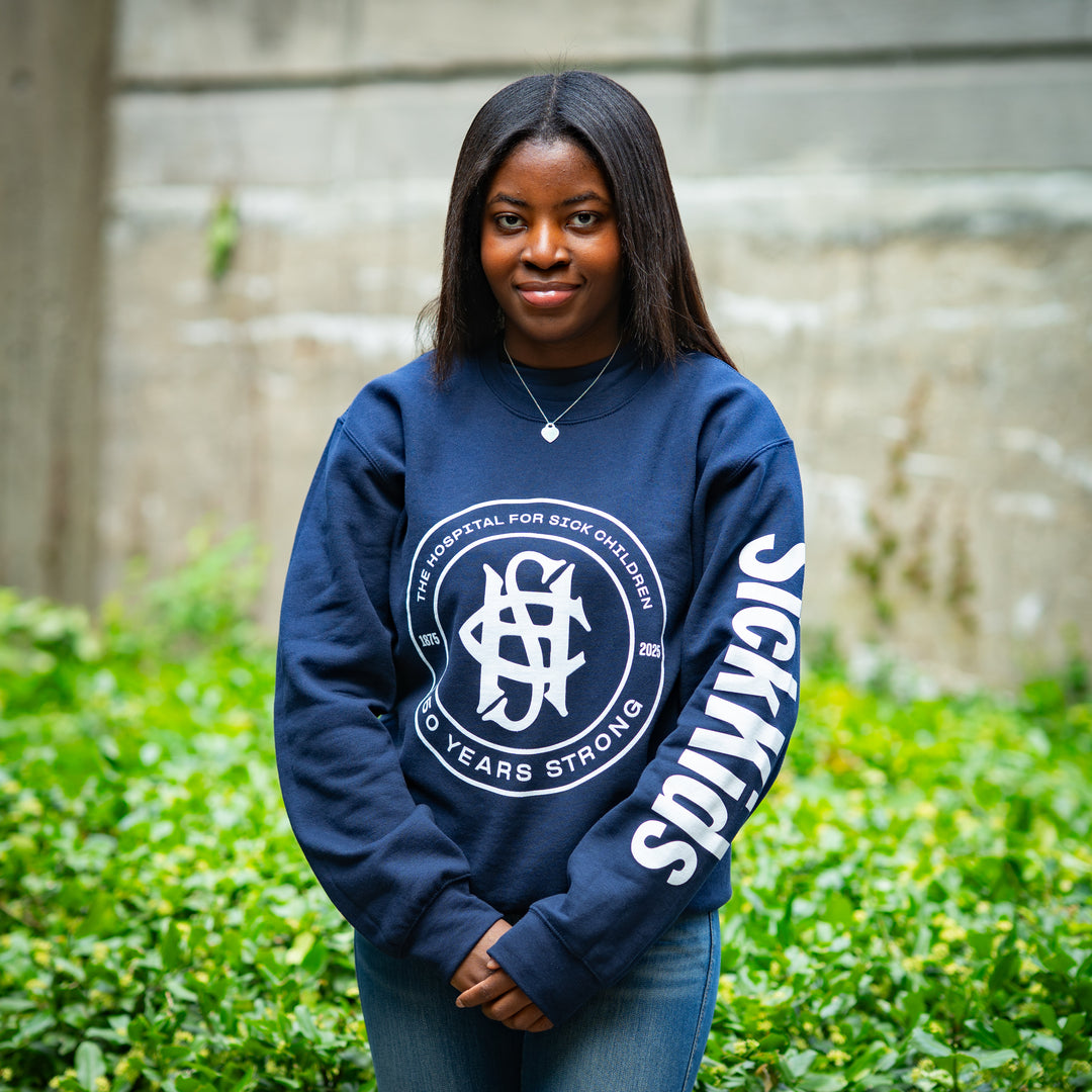 Person wearing a navy blue sweatshirt with a logo and text, standing outdoors.