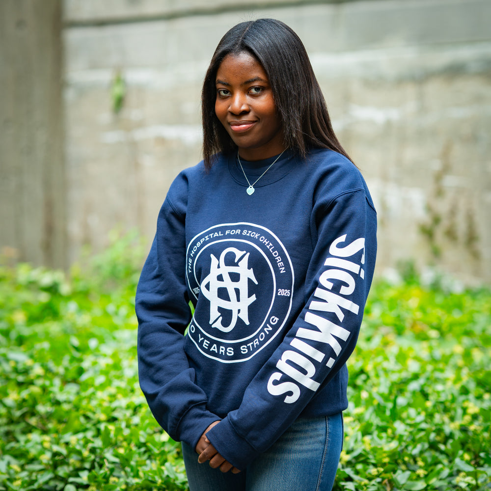 Person wearing a navy blue sweatshirt with a logo and text, standing outdoors.
