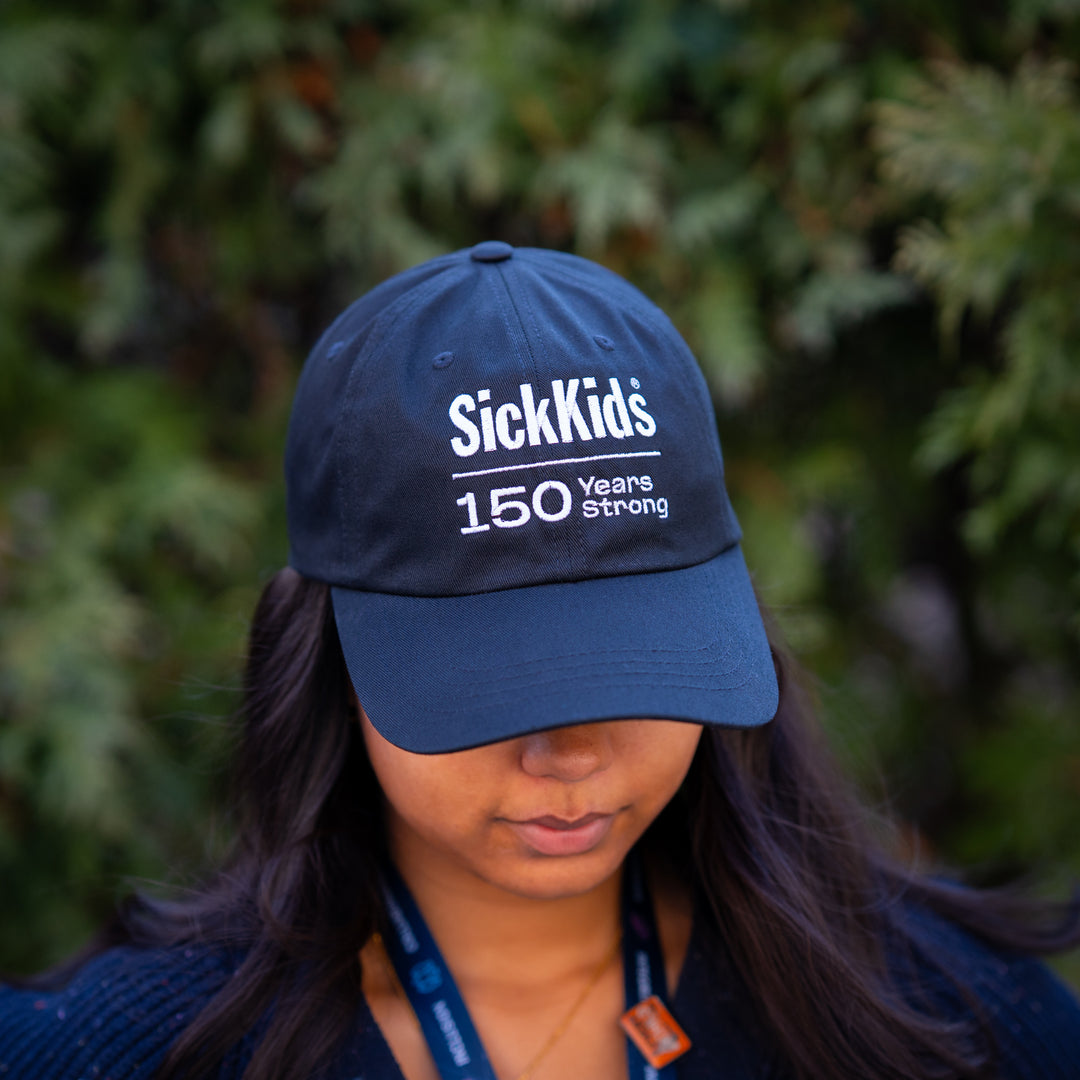 A person wearing a black baseball cap with 'SickKids 150 Years Strong' printed on the front.