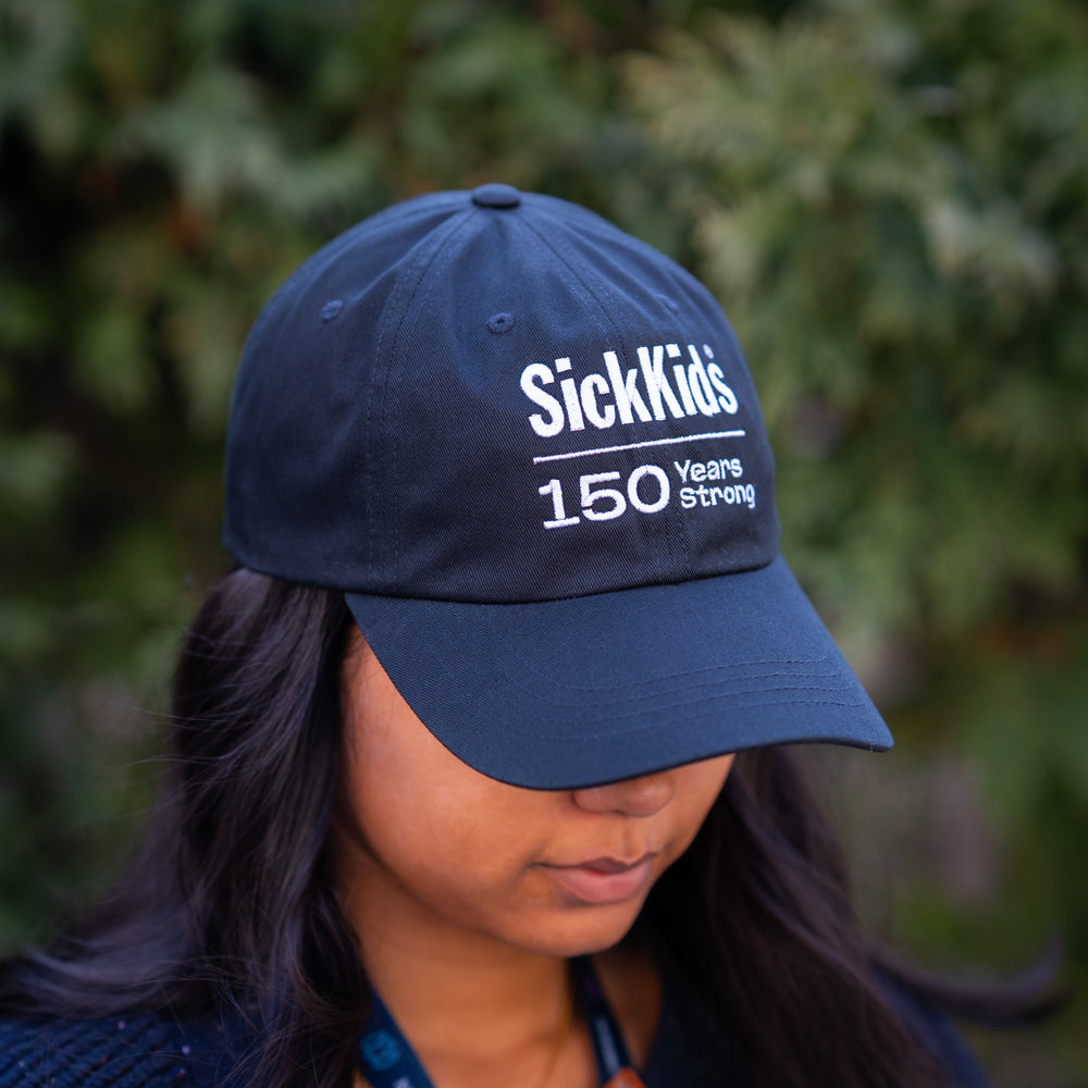 A person wearing a black baseball cap with 'SickKids 150 Years Strong' printed on the front.