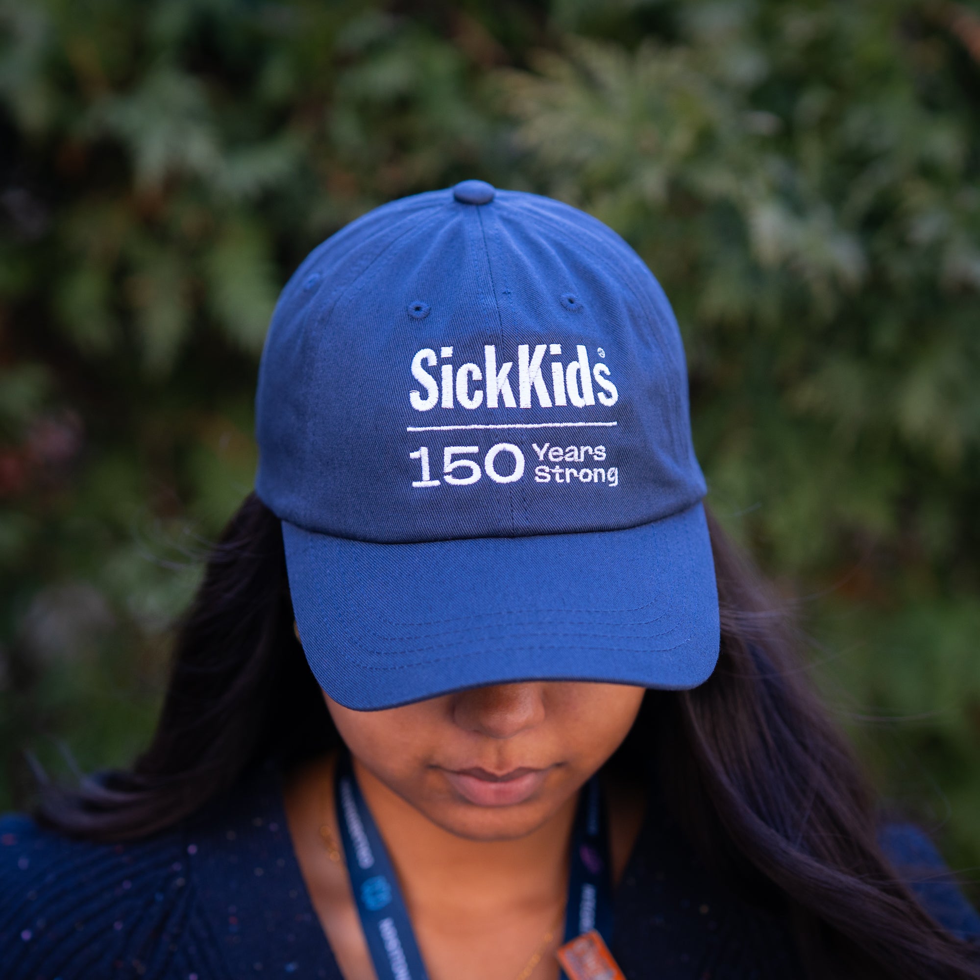 A person wearing a navy blue baseball cap with 'SickKids 150 Years Strong' printed on the front.