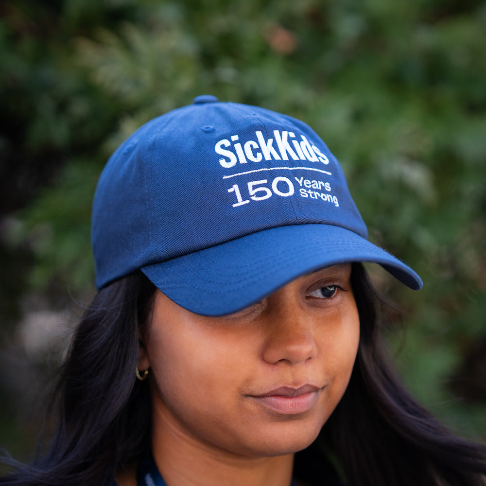 A person wearing a navy blue baseball cap with 'SickKids 150 Years Strong' printed on the front.