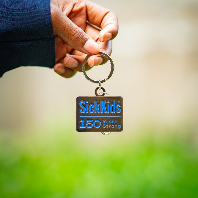 Keychain with 'SickKids 150 Years Strong' text held by a hand against a blurred green background