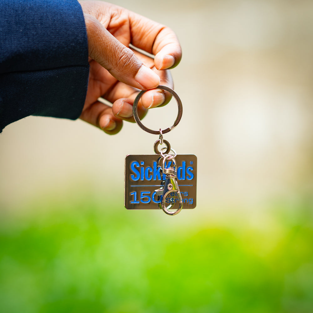 Keychain with 'SickKids 150 Years Strong' text held by a hand against a blurred green background