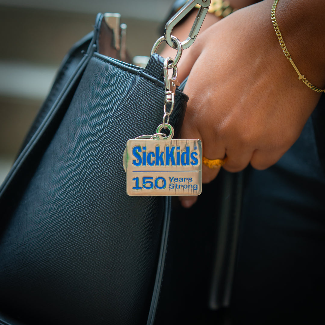 A keychain with a metal clasp and a tag that reads 'SickKids 150 Years Strong' attached to a handbag.