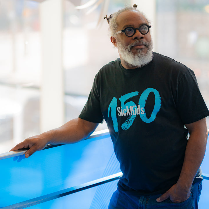 An adult wearing a black t-shirt with the text 'SickKids 150' printed on the front.