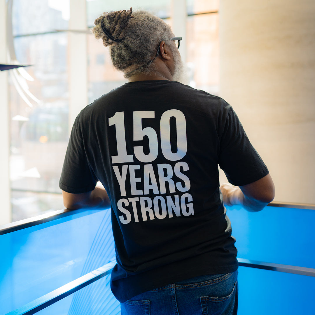 An adult wearing a black t-shirt with the text '150 Years Strong' printed on the back.