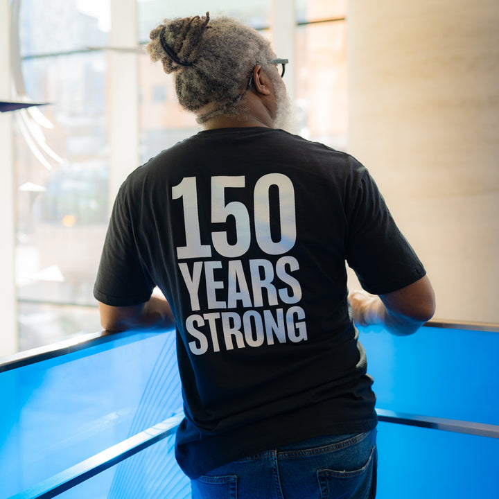 An adult wearing a black t-shirt with the text '150 Years Strong' printed on the back.