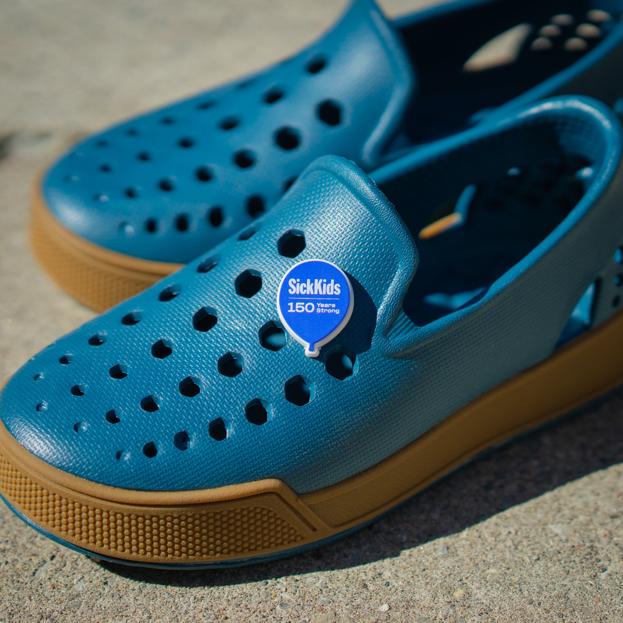 A pair of blue casual shoes with a 'SickKids 150' charm on the upper part.