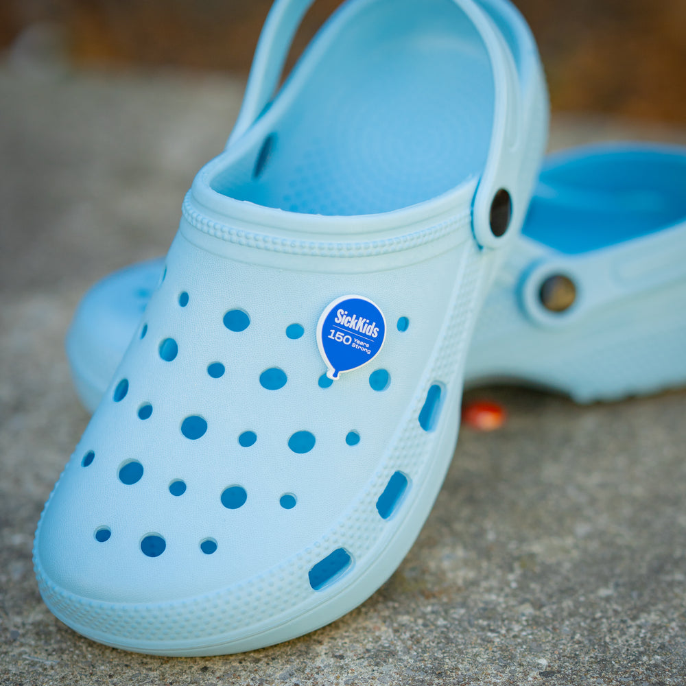 A blue pair of crocs with a SIckKids 150 charm attached to one of them.