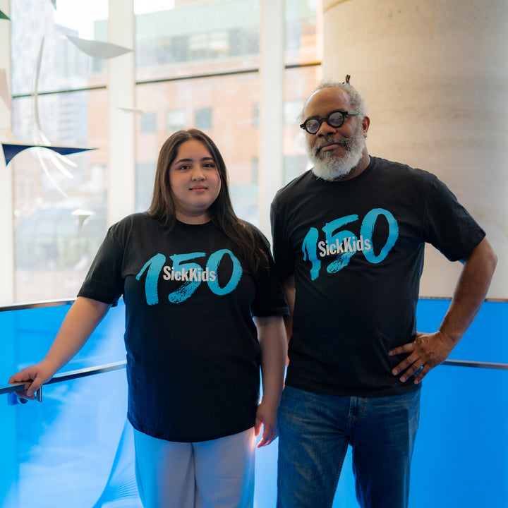 An adult male and an adult female wearing black t-shirts that say "SickKids 150".