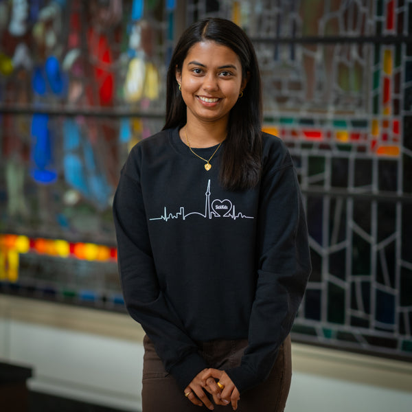 A person wearing a black crewneck sweatshirt with a skyline design in white.