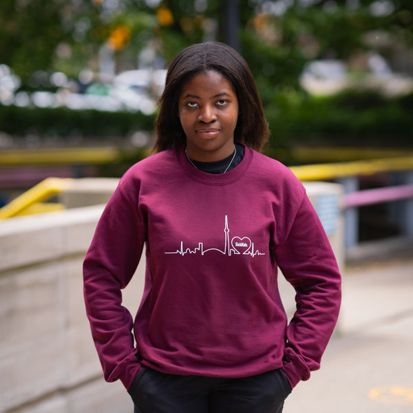 Person wearing a maroon sweatshirt with a design, standing outdoors.