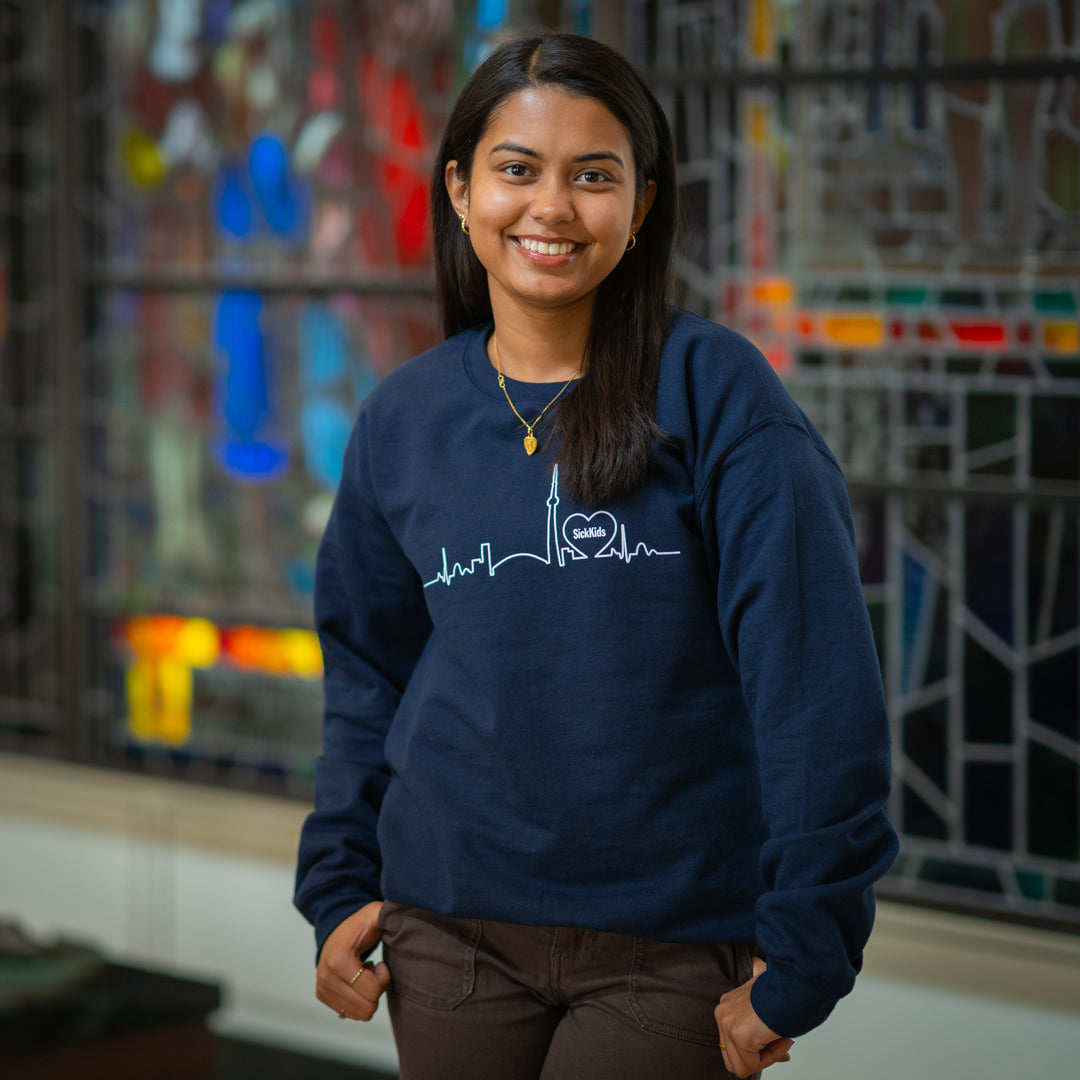 A person wearing a navy blue crewneck sweater with a skyline design on the front.