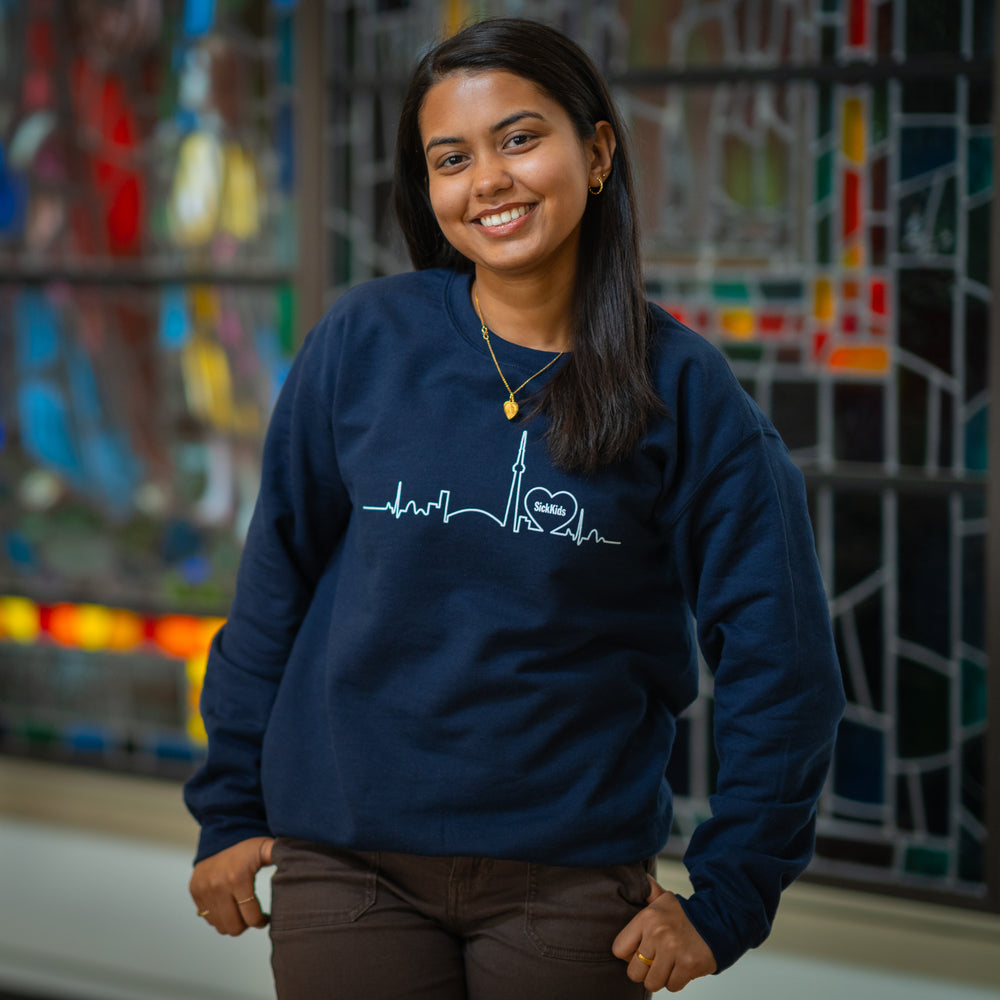 A person wearing a navy blue crewneck sweater with a skyline design on the front.
