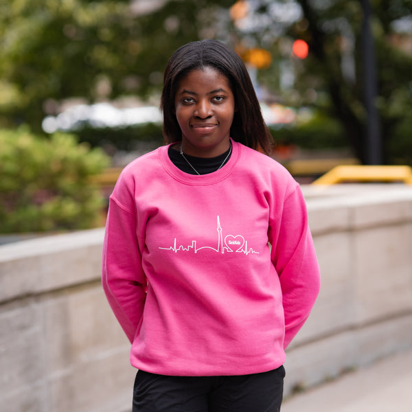 Person wearing a pink sweatshirt with a design on a blurred outdoor background