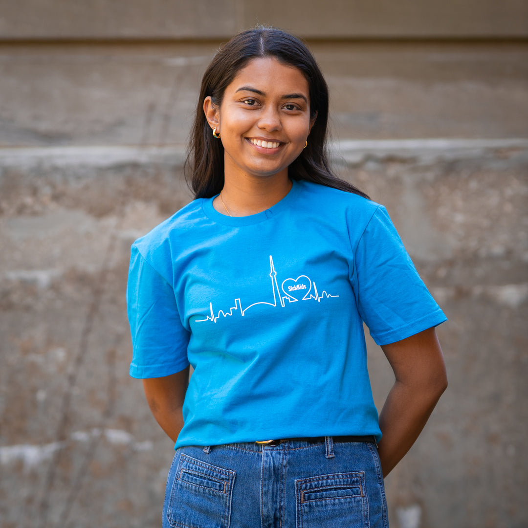 A person wearing a blue t-shirt with a skyline logo in front of a concrete wall.
