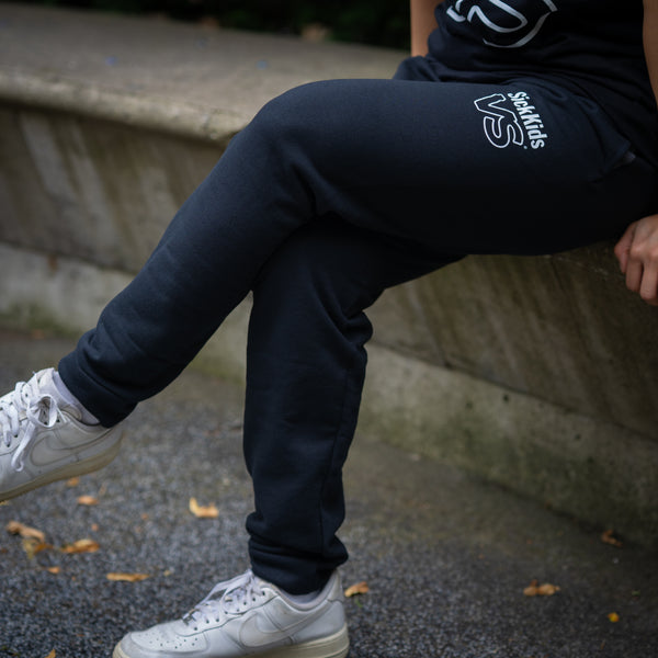 Person wearing black sweatpants with a SickKids VS logo, sitting on a step.