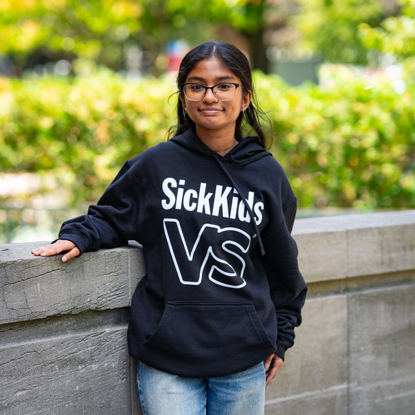 Person wearing a black hoodie with 'SickKids VS' text, standing outdoors.