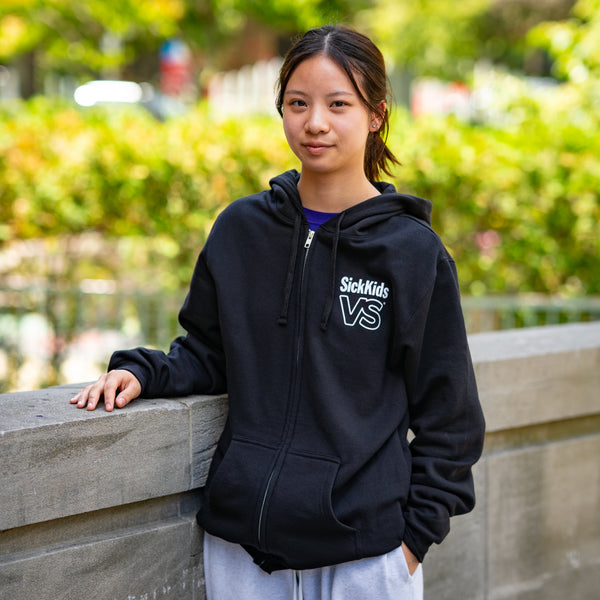 Person wearing a black hoodie with 'SickKids VS' logo, standing outdoors.
