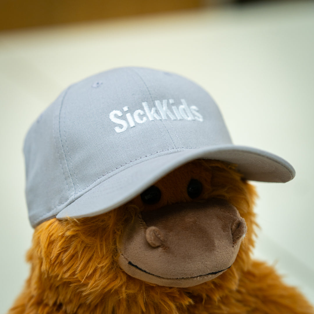 A grey youth baseball cap with the text 'SickKids' displayed on the front, placed on a plush toy.