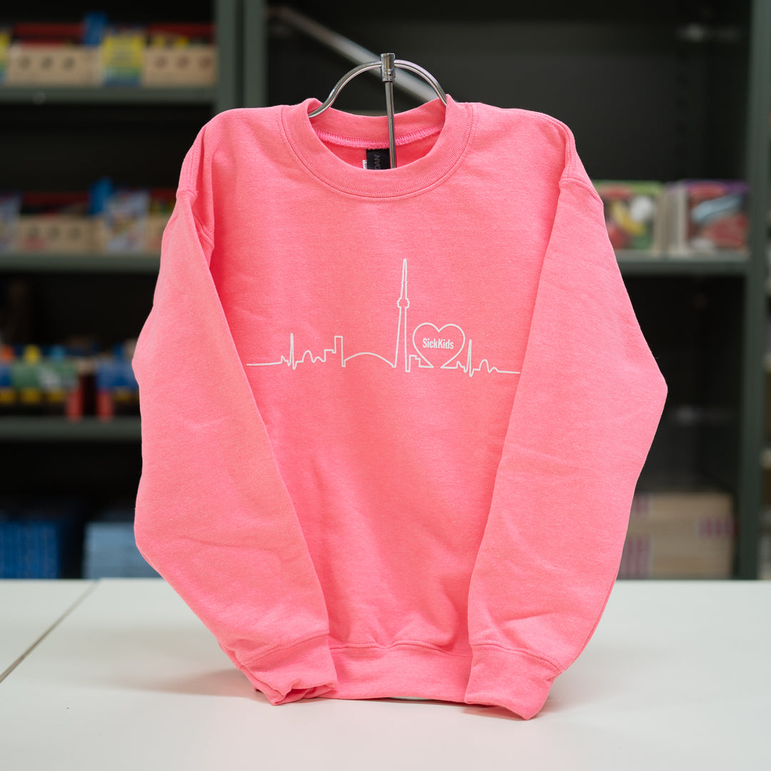 A pink youth crewneck sweater with a skyline print on the front.