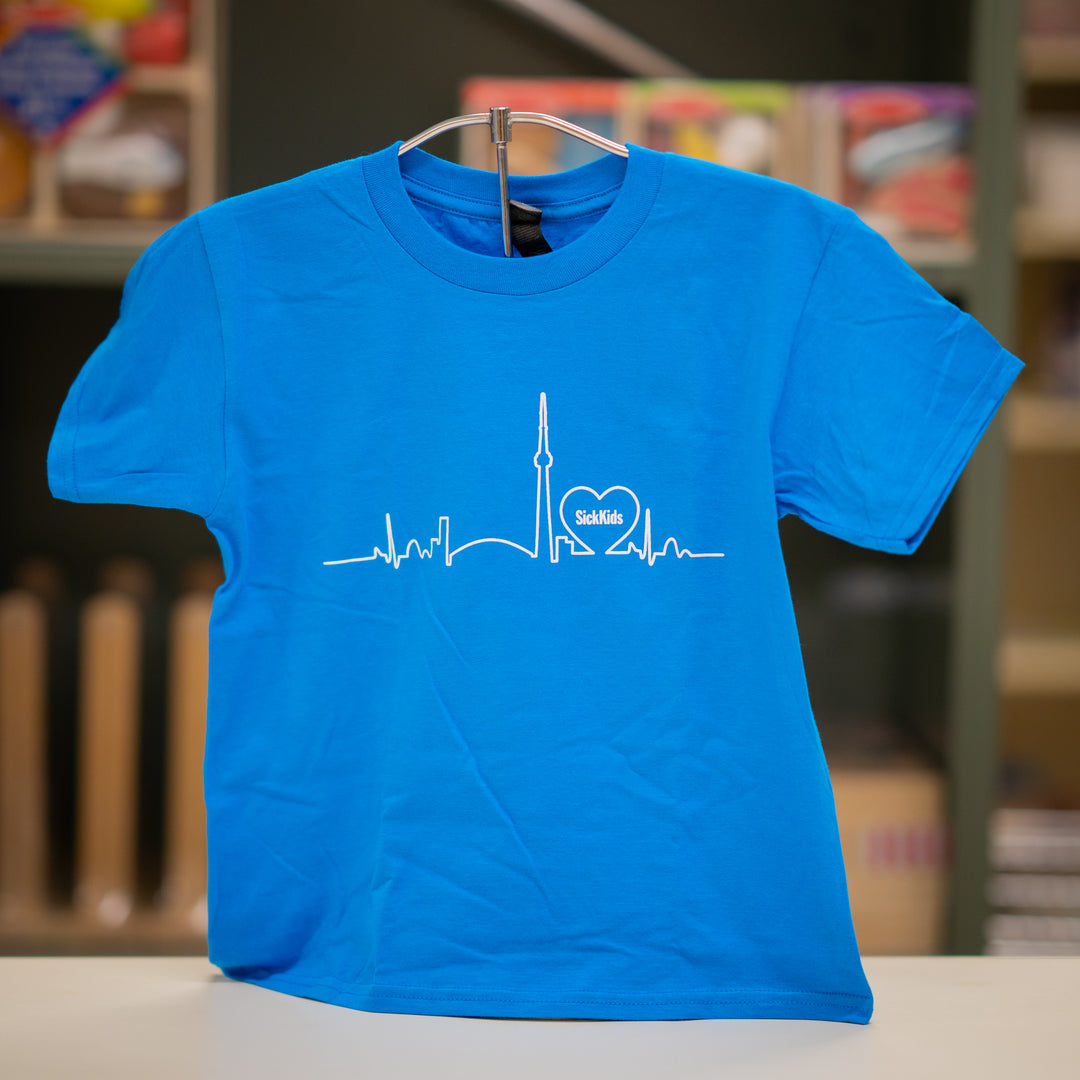 A blue youth T-shirt with a skyline logo on the front, displaying a heartbeat line and the SickKids logo.